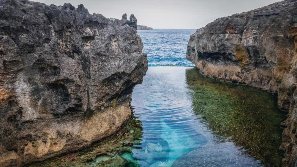 Scenic overview of Angel Billabong Nusa Penida featuring crystal clear turquoise natural infinity pool surrounded by dramatic limestone cliffs and unique rock formations, accessible via Axe Stone Fast Cruise from Sanur Harbour to West Nusa Penida Tour