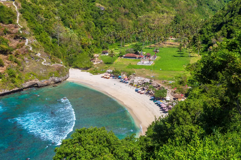 Scenic panoramic view of Atuh Beach on a West Nusa Penida Tour with Axestone Fast Cruise, featuring dramatic limestone cliffs, white sand shoreline, and crystal clear turquoise waters.