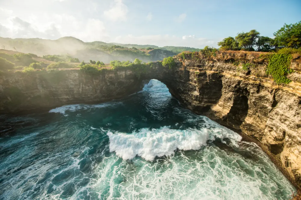Scenic overview of Broken Beach natural rock arch formation in West Nusa Penida Tour with Axestone Fast Cruise, featuring turquoise water inside circular cliff walls and dramatic coastal scenery