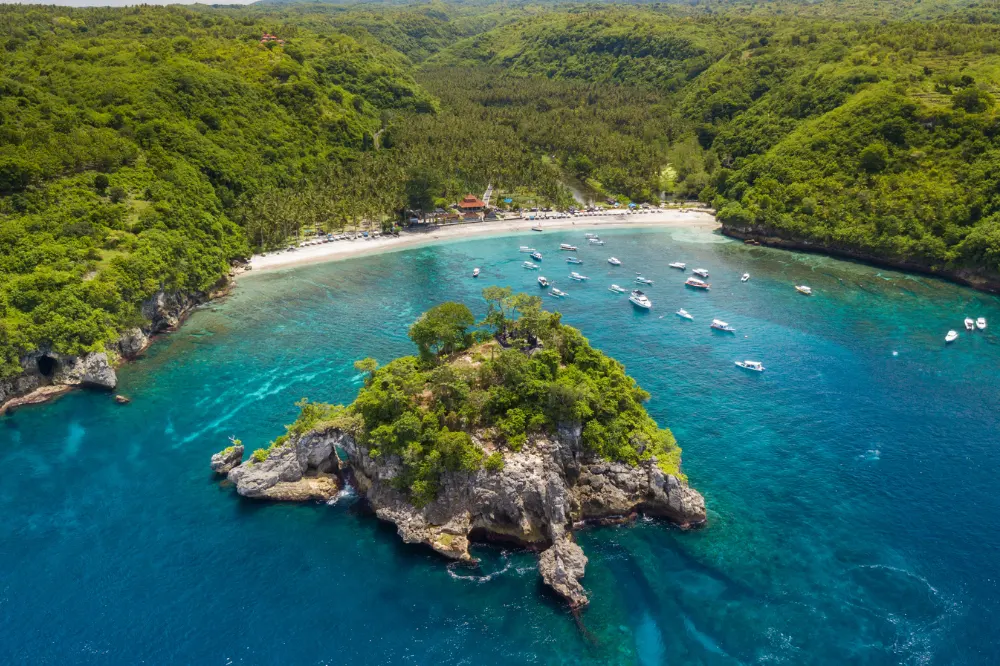 Scenic panoramic view of Crystal Bay's white sand beach and turquoise waters on a West Nusa Penida Tour with Axestone Fast Cruise, surrounded by lush green hills and palm trees