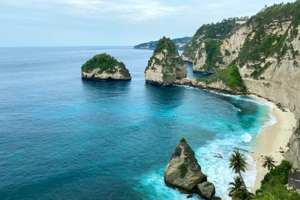 Panoramic view of Diamond Beach in East Nusa Penida during an East Nusa Penida Tour by Axestone Fast Cruise, showcasing white sand and crystal clear turquoise water.