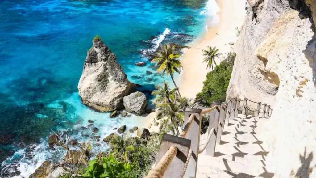 Popular stairs photo spot at Diamond Beach Nusa Penida overlooking turquoise waters and white sand against dramatic cliff backdrop, a must-visit Instagrammable location on East Nusa Penida Tour packages with Axe Stone Fast Cruise daily departures