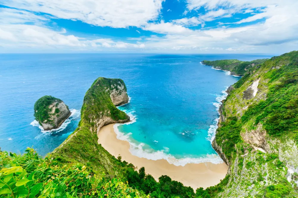 Breathtaking aerial view of Kelingking Beach cliff in West Nusa Penida Tours by Axestone Fast Cruise, featuring the iconic T-Rex shaped coastline and turquoise bay.