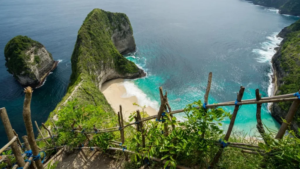 Pristine white sand beach at Kelingking Beach Nusa Penida framed by towering limestone cliffs and crystal clear turquoise waters (swimming not recommended due to strong currents), a rewarding destination for adventurous travelers booking Nusa Penida tours with Axe Stone Fast Cruise from Sanur