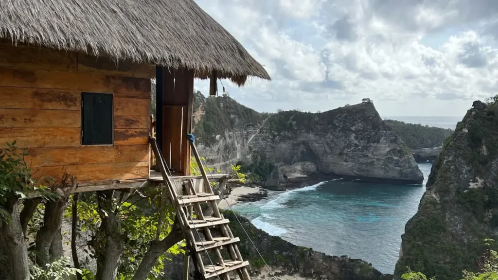 Iconic wooden Tree House Nusa Penida (Rumah Pohon Molenteng) perched on 50-meter cliff with staircase leading to entrance overlooking turquoise ocean, a must-visit Instagrammable photo spot on East Nusa Penida Tour with Axe Stone Fast Cruise from Sanur Harbour
